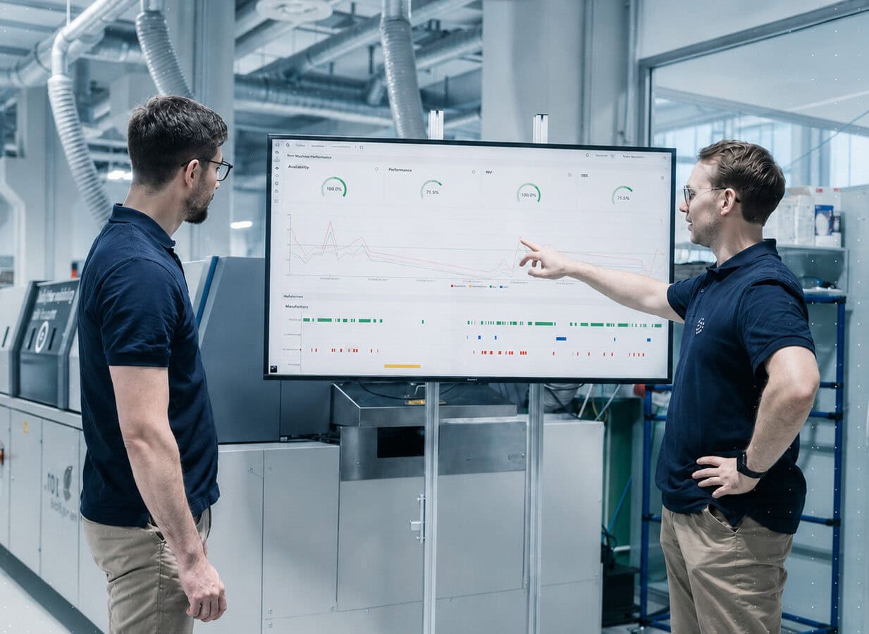 Zwei Techniker analysieren Daten auf einem Bildschirm in einer Fertigungsanlage.
